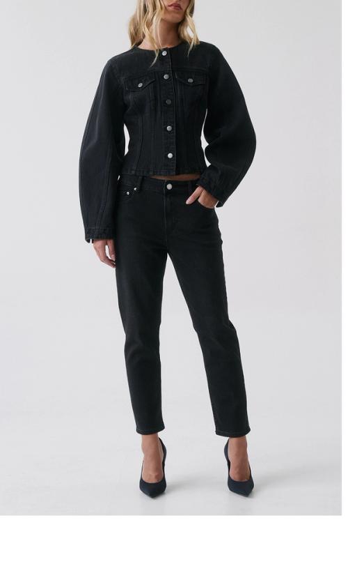 Woman standing in front of a white wall wearing a matching black denim jacket and jeans.