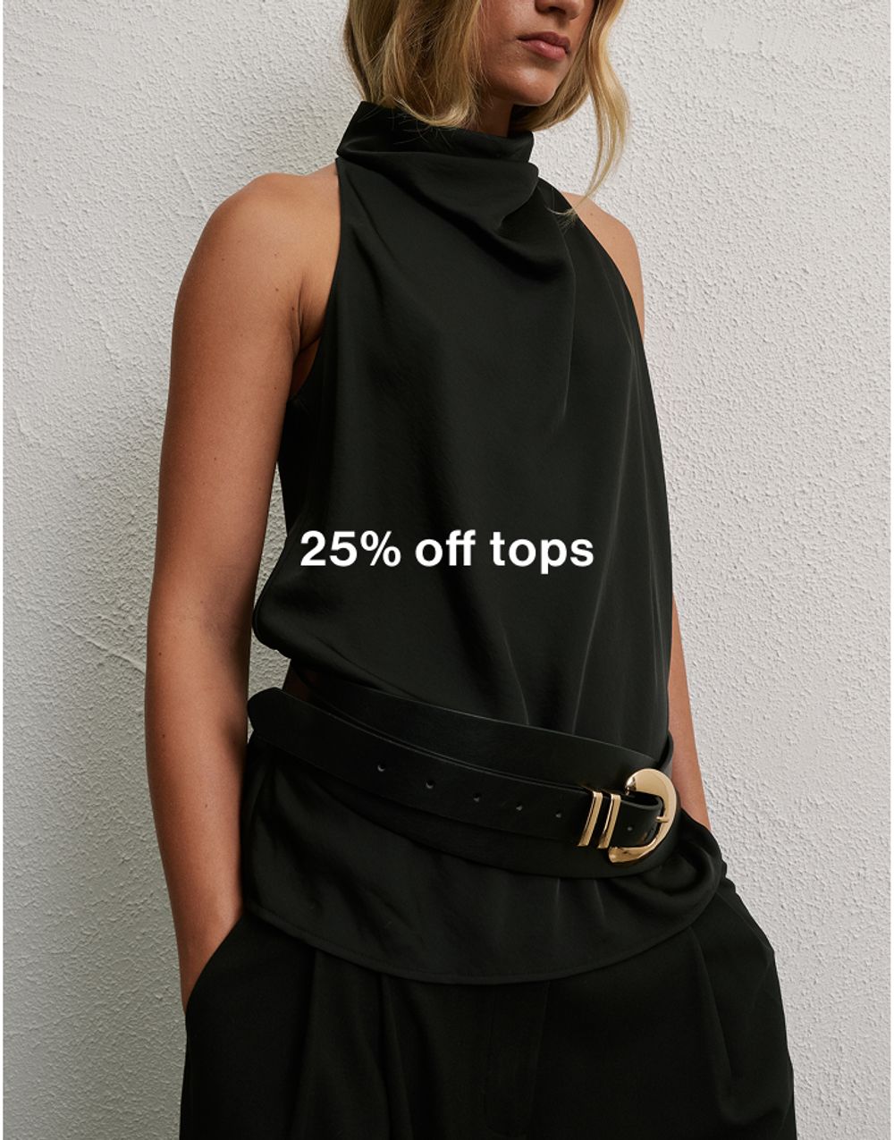 Woman wearing a black turtle neck top standing in front of a white wall with text that states 25% off tops