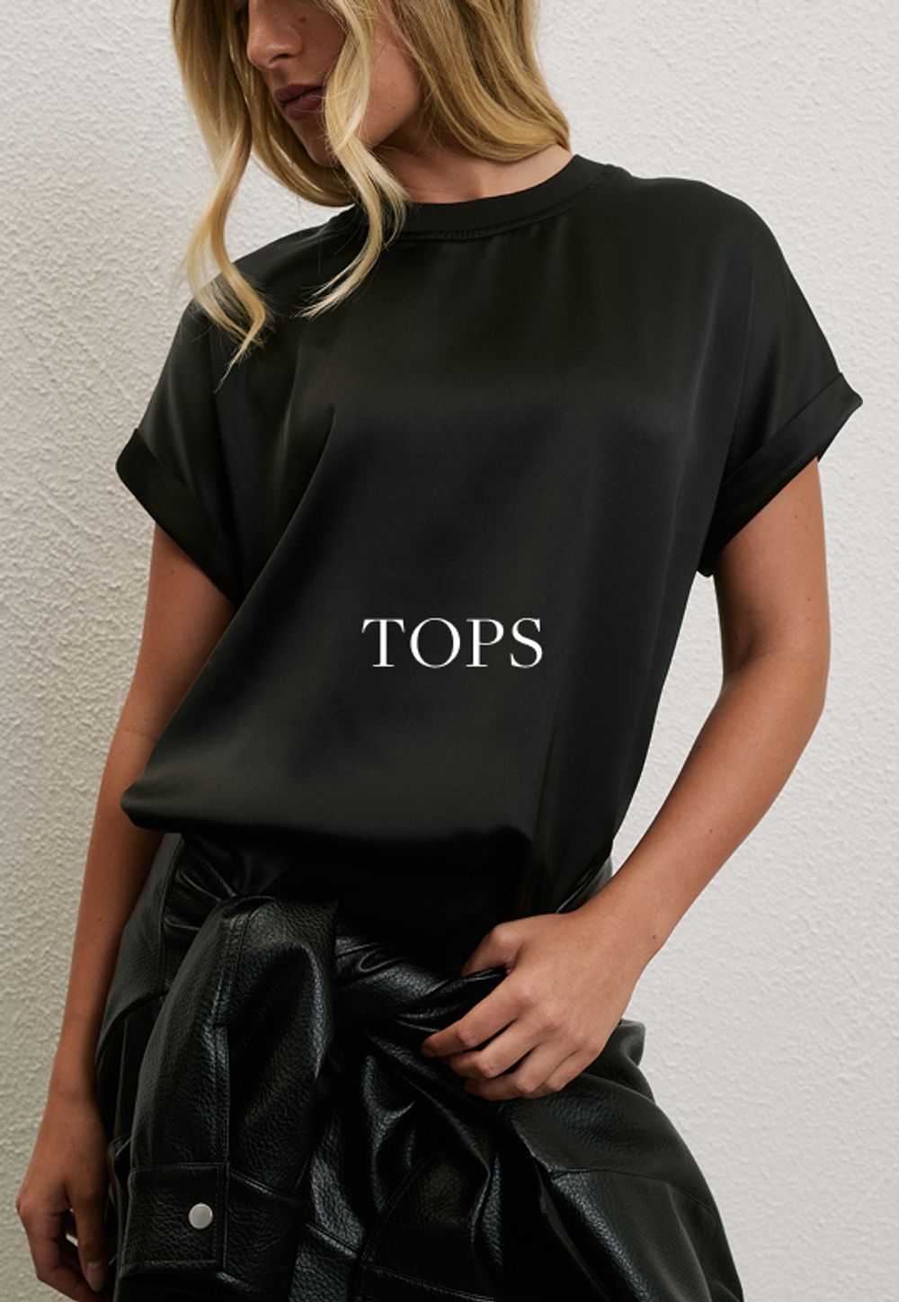 Woman standing in front of a white wall wearing a plum short sleeve satin top and sequin skirt with text overlay which states "Tops"