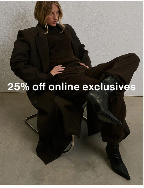 Woman posing in front of a white wall wearing a black long coat, sitting on a modern chair with text overlay which states "25%off knits"