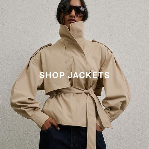 Woman posing in front of a white wall wearing brown leather jacket and sunglasses with text overlay that says "SHOP JACKETS"