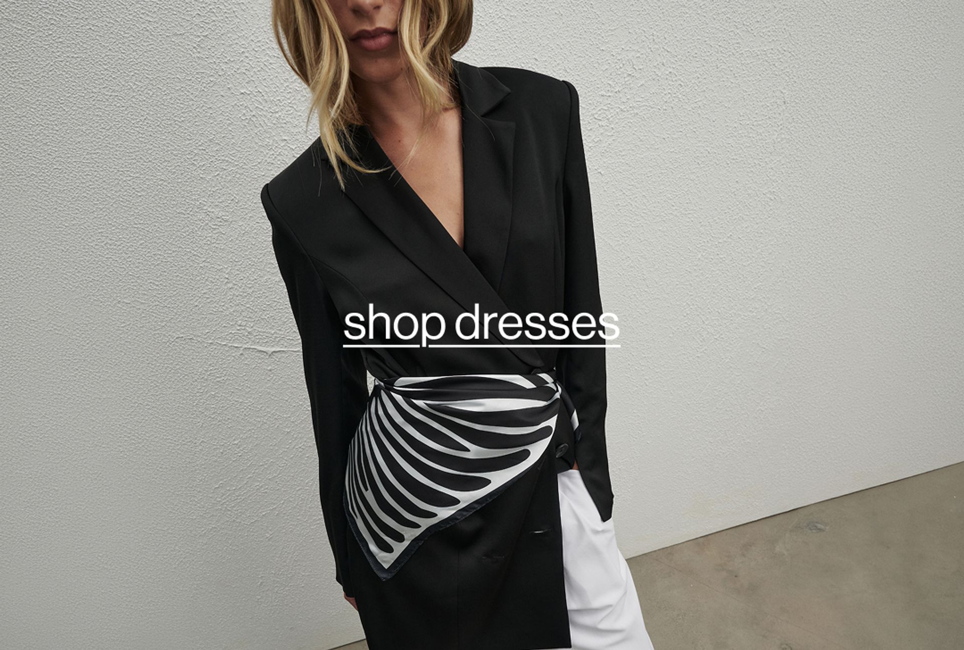 Woman posing in front of a white wall with text that reads "shop dresses" 