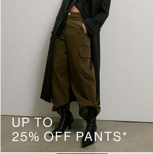 Woman wearing a long black coat, green pants and boots standing in front of a white wall with text that states 25% off pants