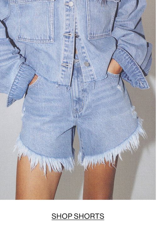 Woman posing with her hands in her pockets wearing denim shorts with text overlay "SHOP SHORTS"