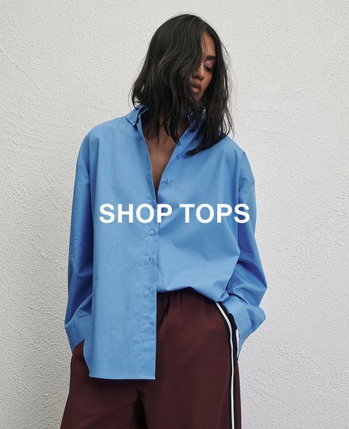 Woman standing in front of a white wall wearing a blue long sleeve shirt with text overlay which states "20% off Tops"