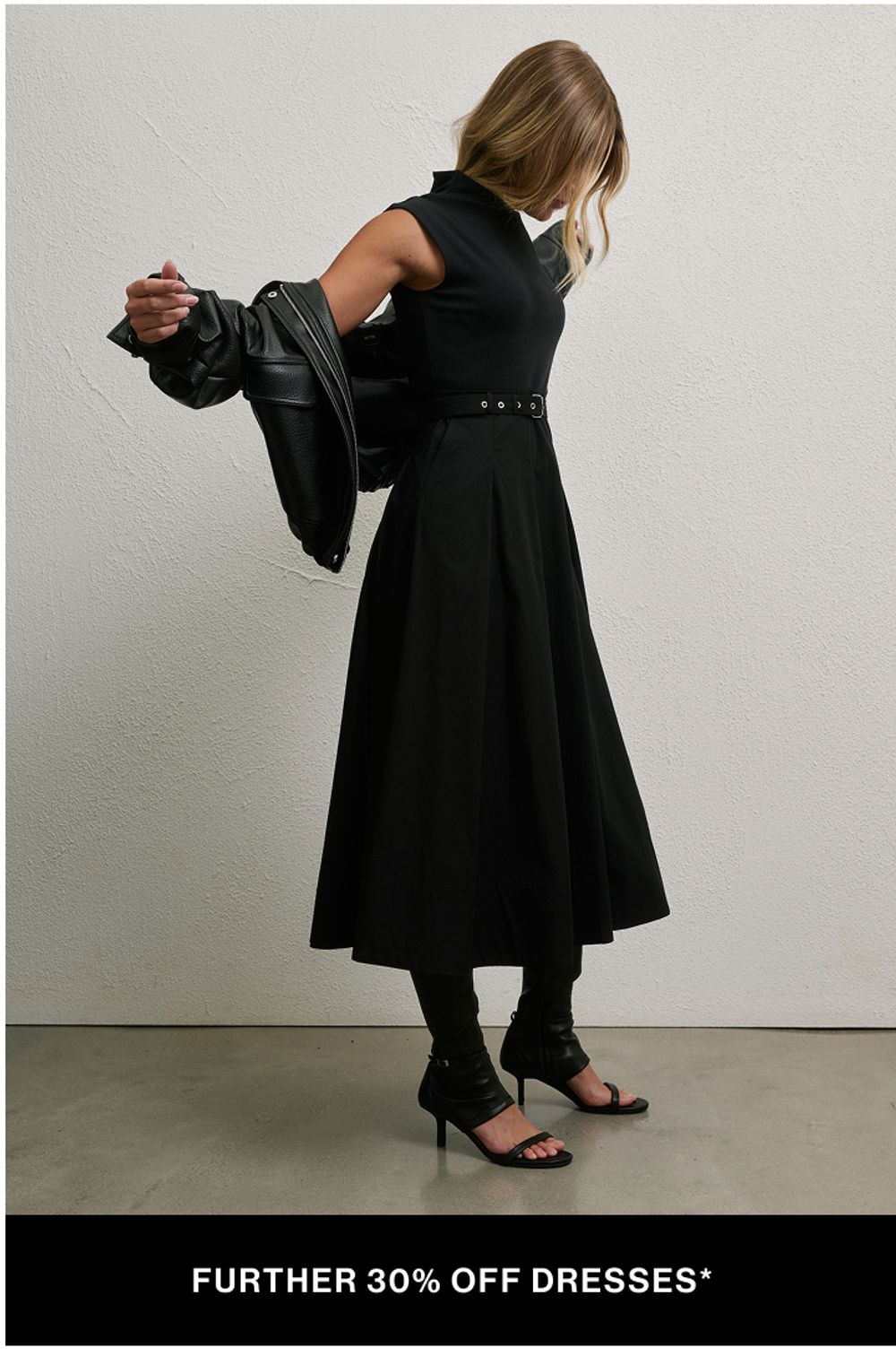 Woman standing in front of a white wall wearing a black dress and leather jacket with text overlay which states "further 20% off dresses"