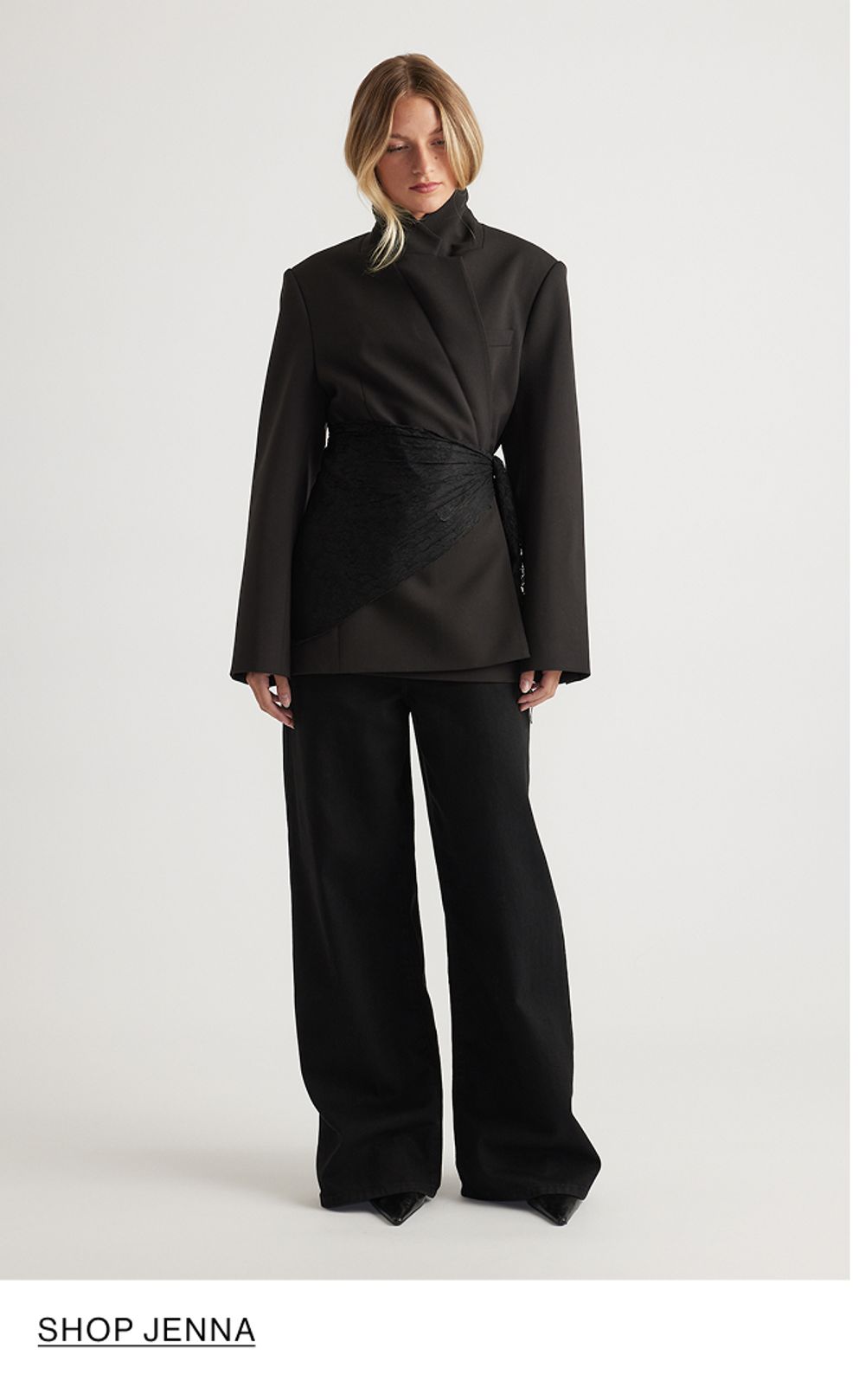 Woman standing looking down wearing a black blazer and black jeans with text that reads "Shop Jenna"