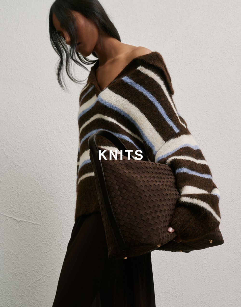 Model standing on her side wearing a stripey jumper and holding a brown bag which has text overlay knits