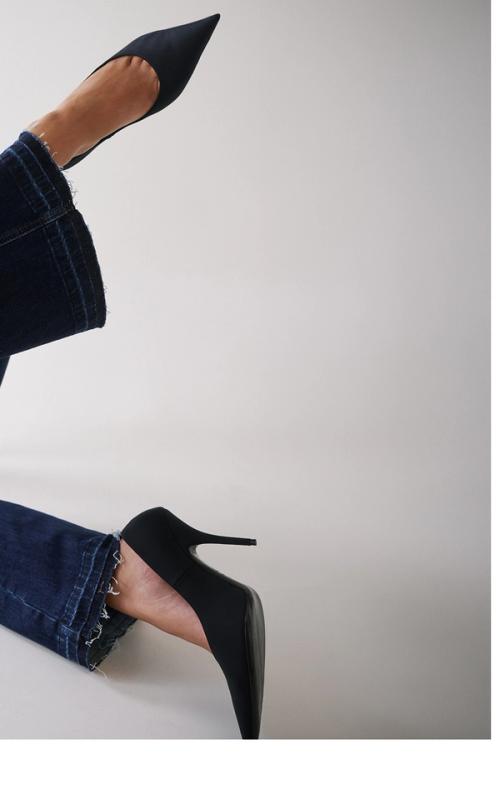 Woman posing in a modern stance, wearing a matching double denim set with pointed black heels.