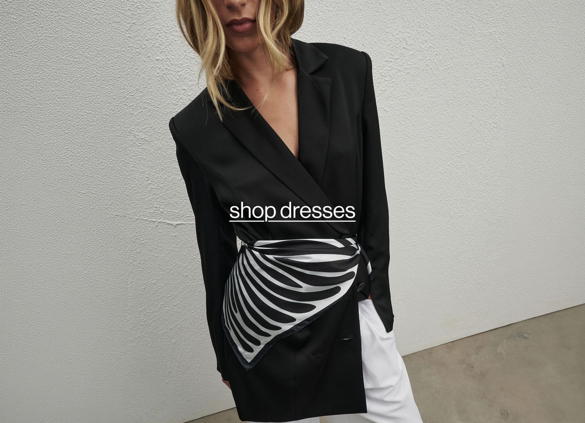 Woman posing in front of a white wall with text that reads "shop dresses" 