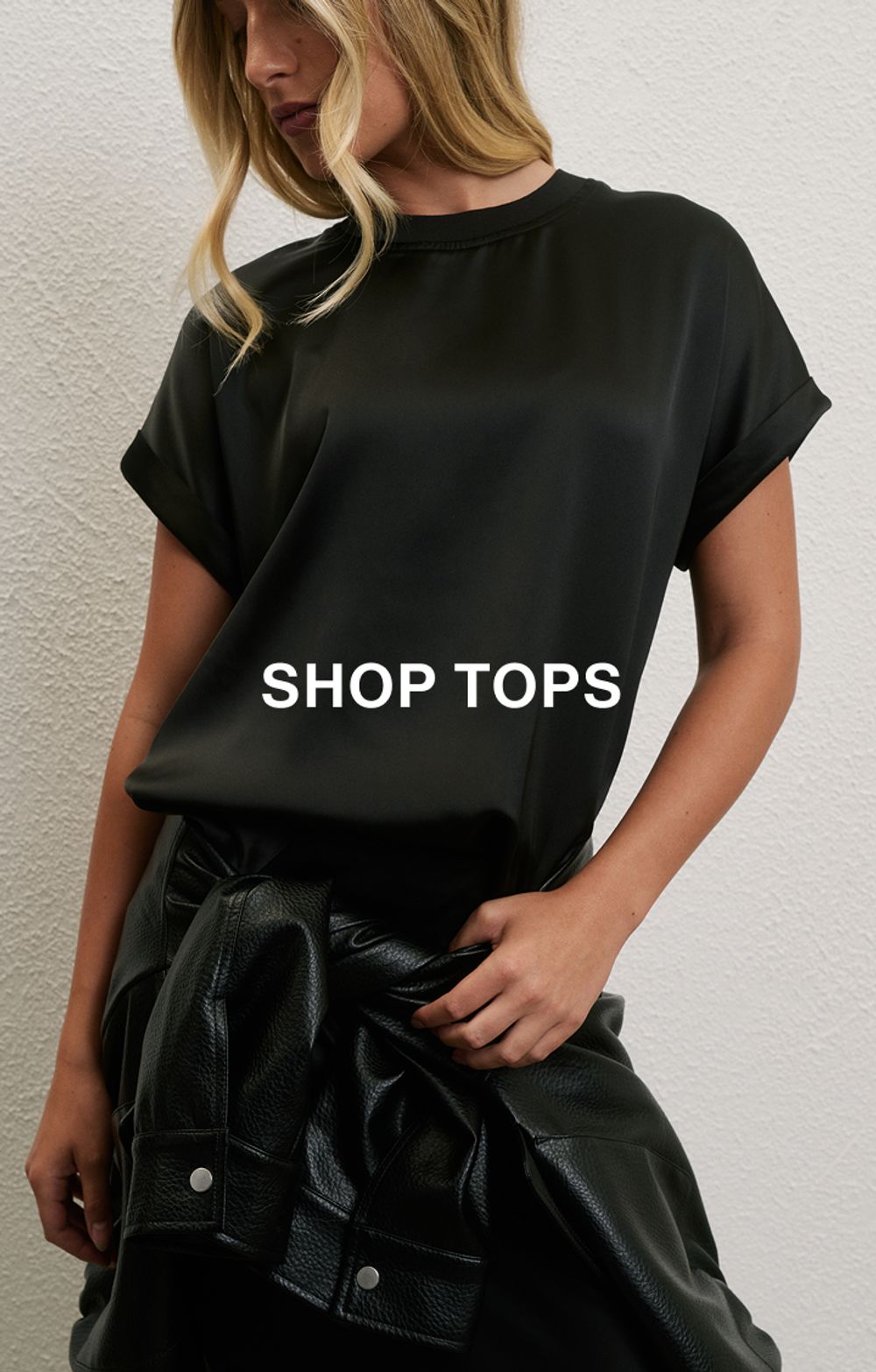 Woman posing in front of a white wall wearing a jeans and a black long sleeve top with text that states "20% off all denim"