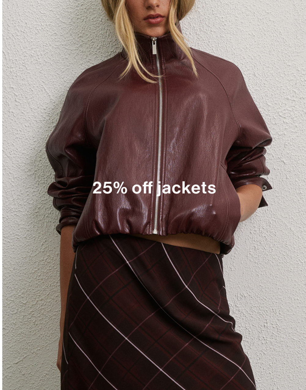 Woman posing in front of a white wall wearing burgundy jacket with text that states "25% off jackets"