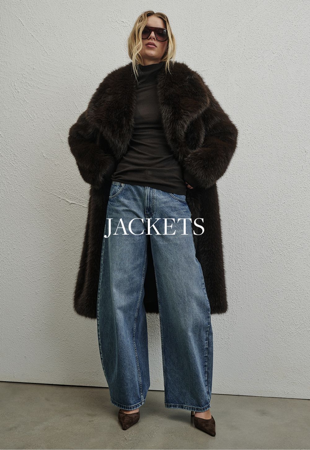 Woman standing in front of a white wall wearing fur coat and sunglasses with text overlay which states "Jackets"