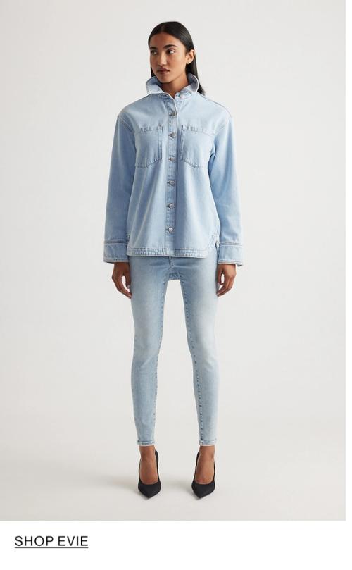 Woman standing in front of a white wall wearing a matching denim jacket and jeans set with texts that reads shop Evie