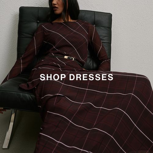Woman posing in a modern chair wearing a checkered dress with text overlay that says "SHOP DRESSES"