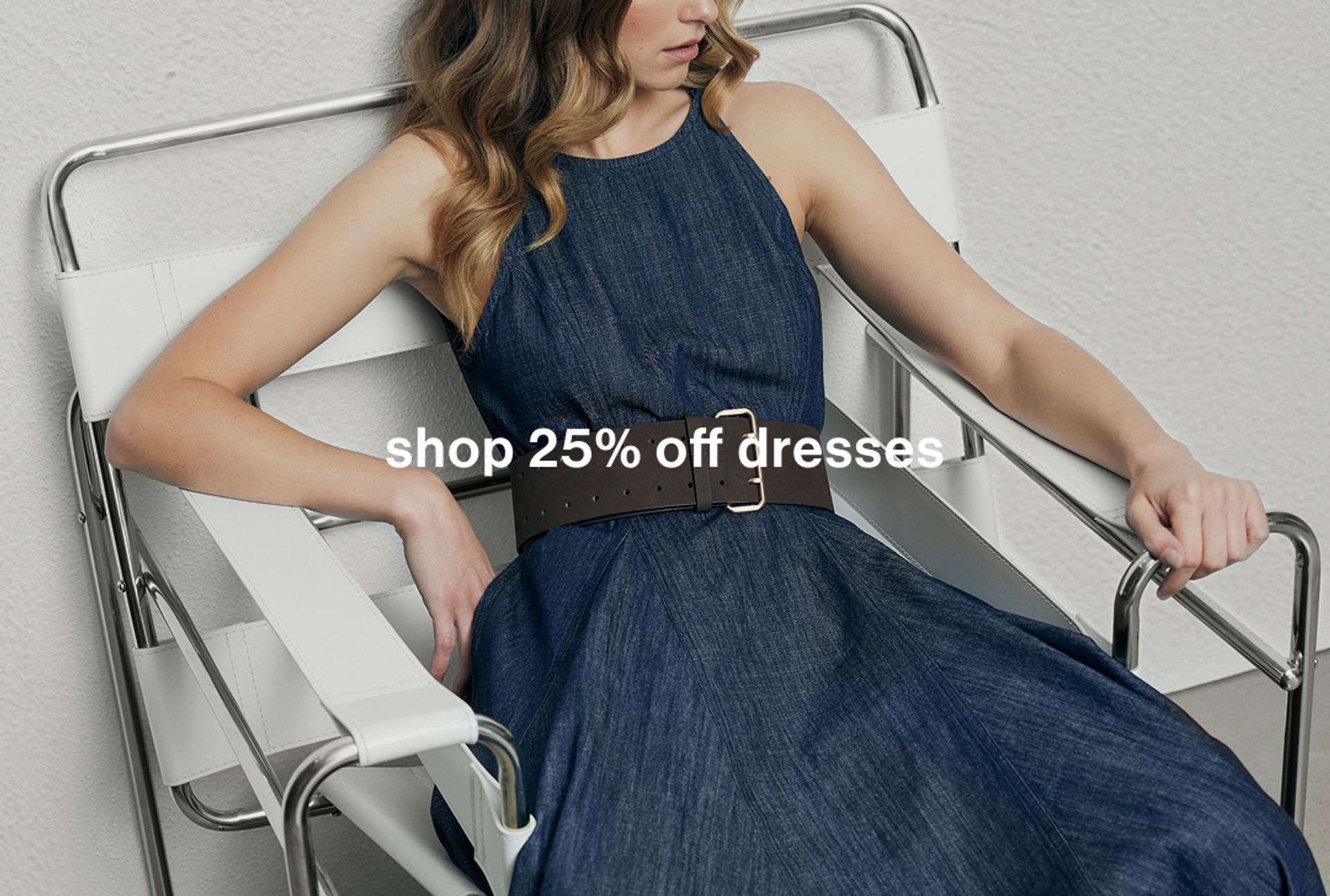 Woman wearing a blue long dress with a belt, seated in a modern chair. Text reads "shop 25% off dresses."
