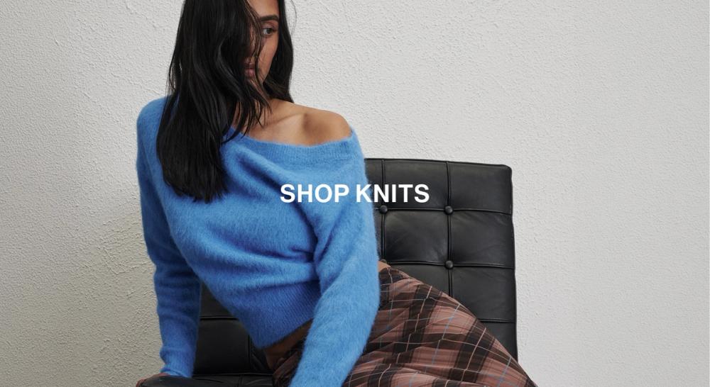 Woman in a blue knit in front of a white wall with text that reads "20% off all Knits"