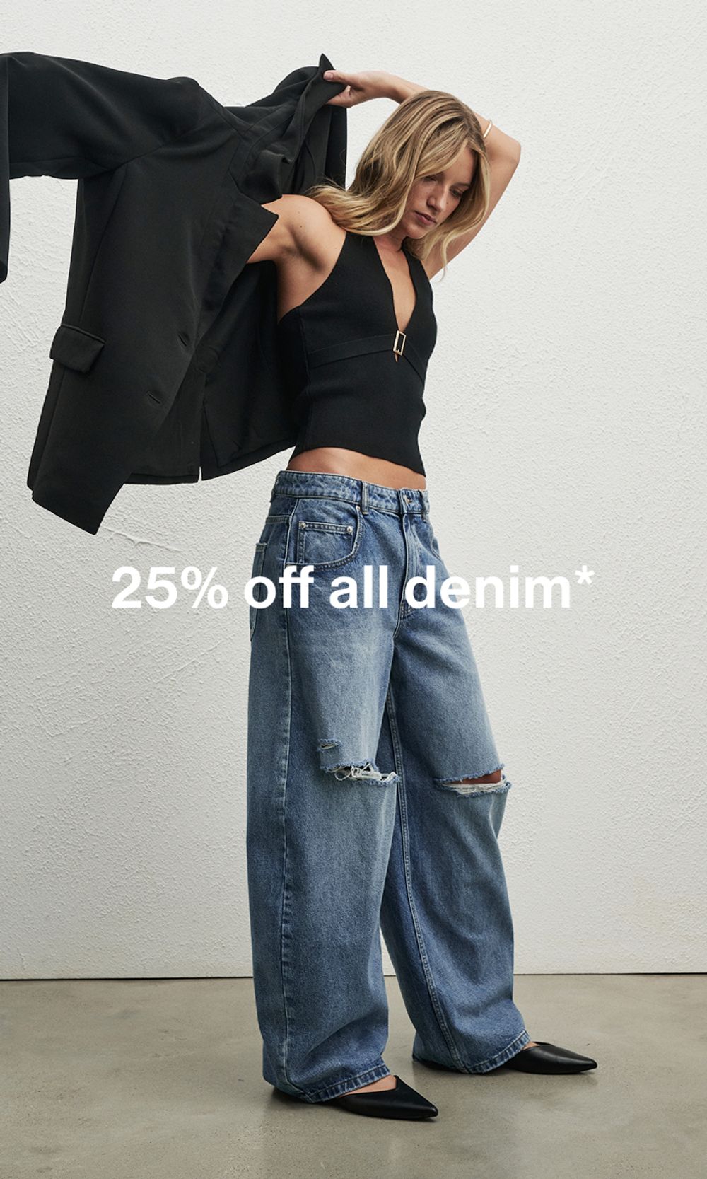 Model in a black top and denim jeans, standing casually. Text reads ‘25% off all denim'