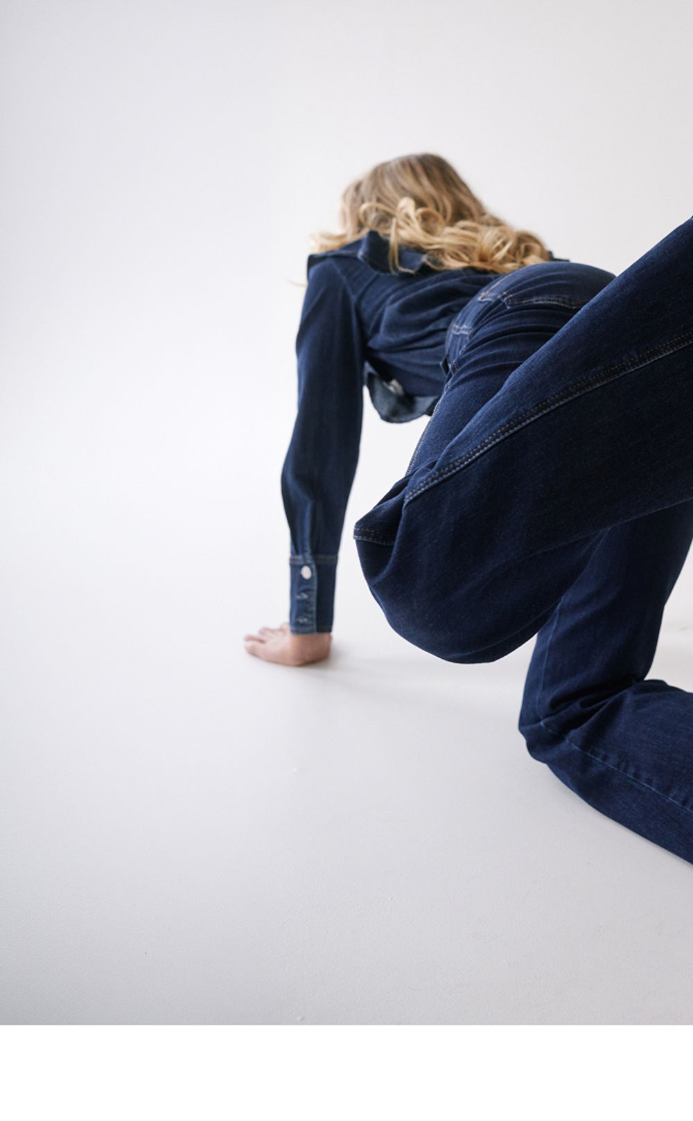 Woman posing in a modern stance, wearing a matching double denim set with pointed black heels.