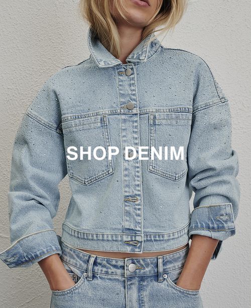 Woman posing in front of a white wall wearing a jeans and a black long sleeve top with text that states "20% off all denim"
