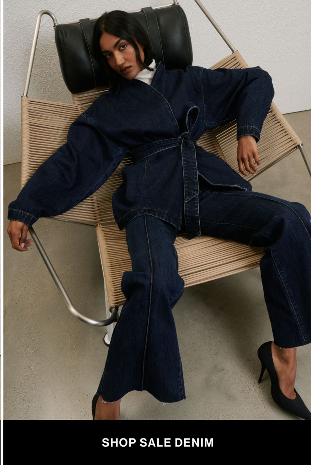 Woman sitting in a modern chair wearing double denim with text overlay which states "further 20% off denim"