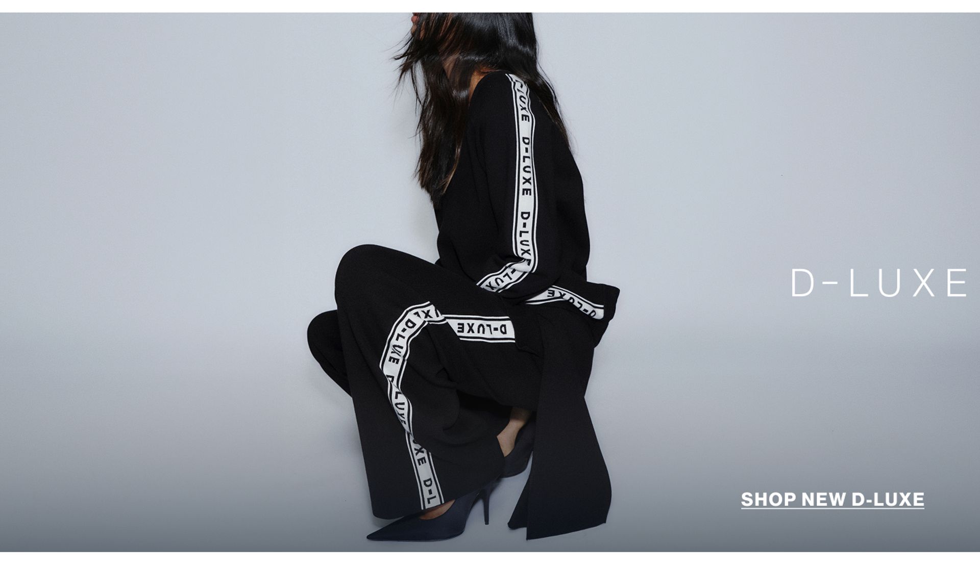 Model in a leather jacket standing in front of a white wall with text overlay which states "20% OFF DLUXE BASICS"