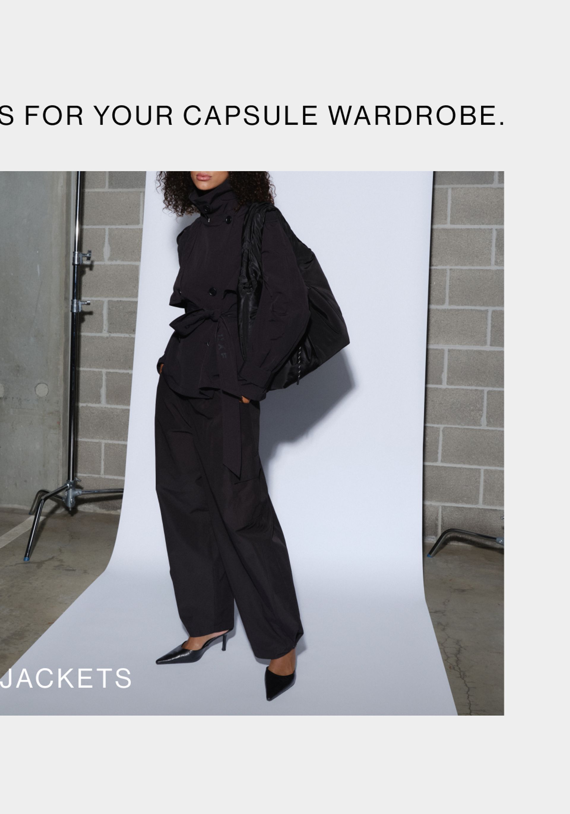 Woman posing in front of a white wall wearing a black jacket with text that states "jackets"