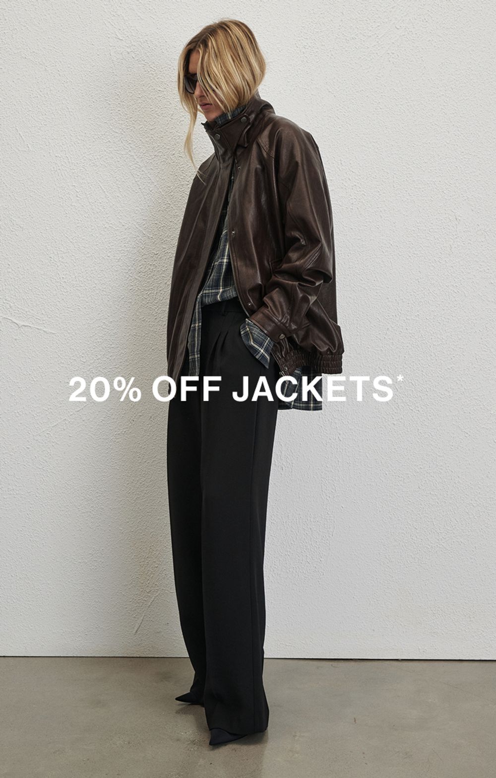 Woman sitting in front of a white wall wearing brown jacket with text overlay which states "20% off all Jackets"