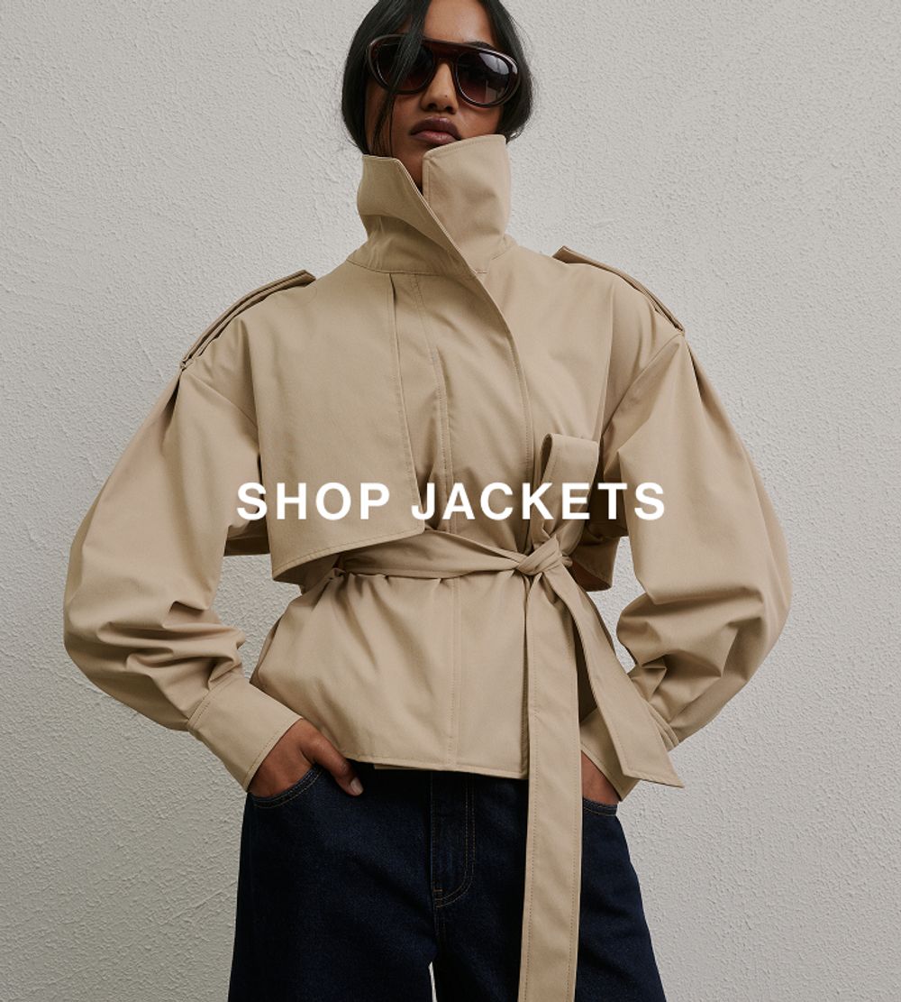 Woman posing in front of a white wall wearing brown leather jacket and sunglasses with text overlay that says "SHOP JACKETS"