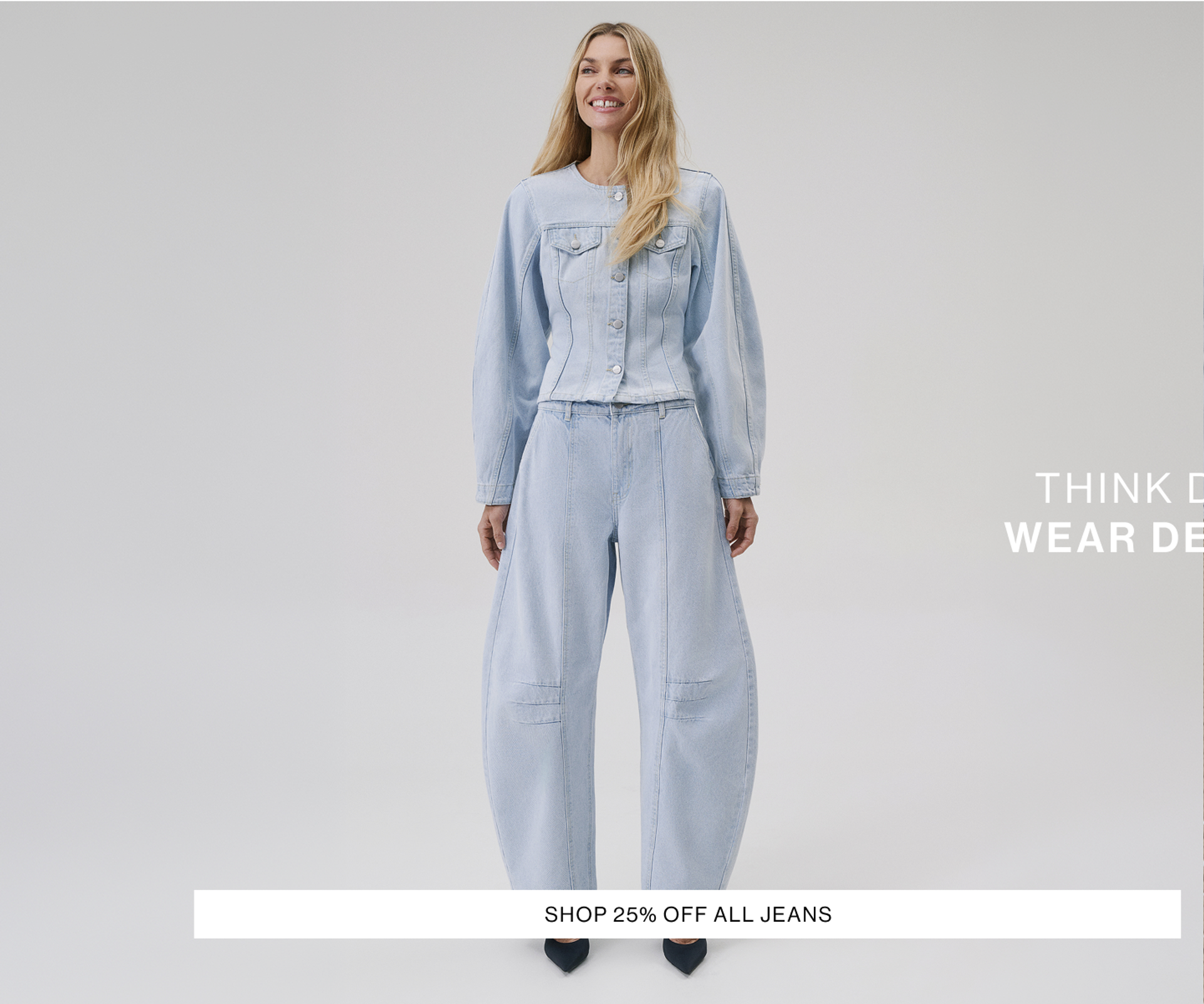 Woman staring at the camera laying in a modern chair wearing a matching denim set. Text reads 'think denim wear decjuba, shop 25% off all jeans