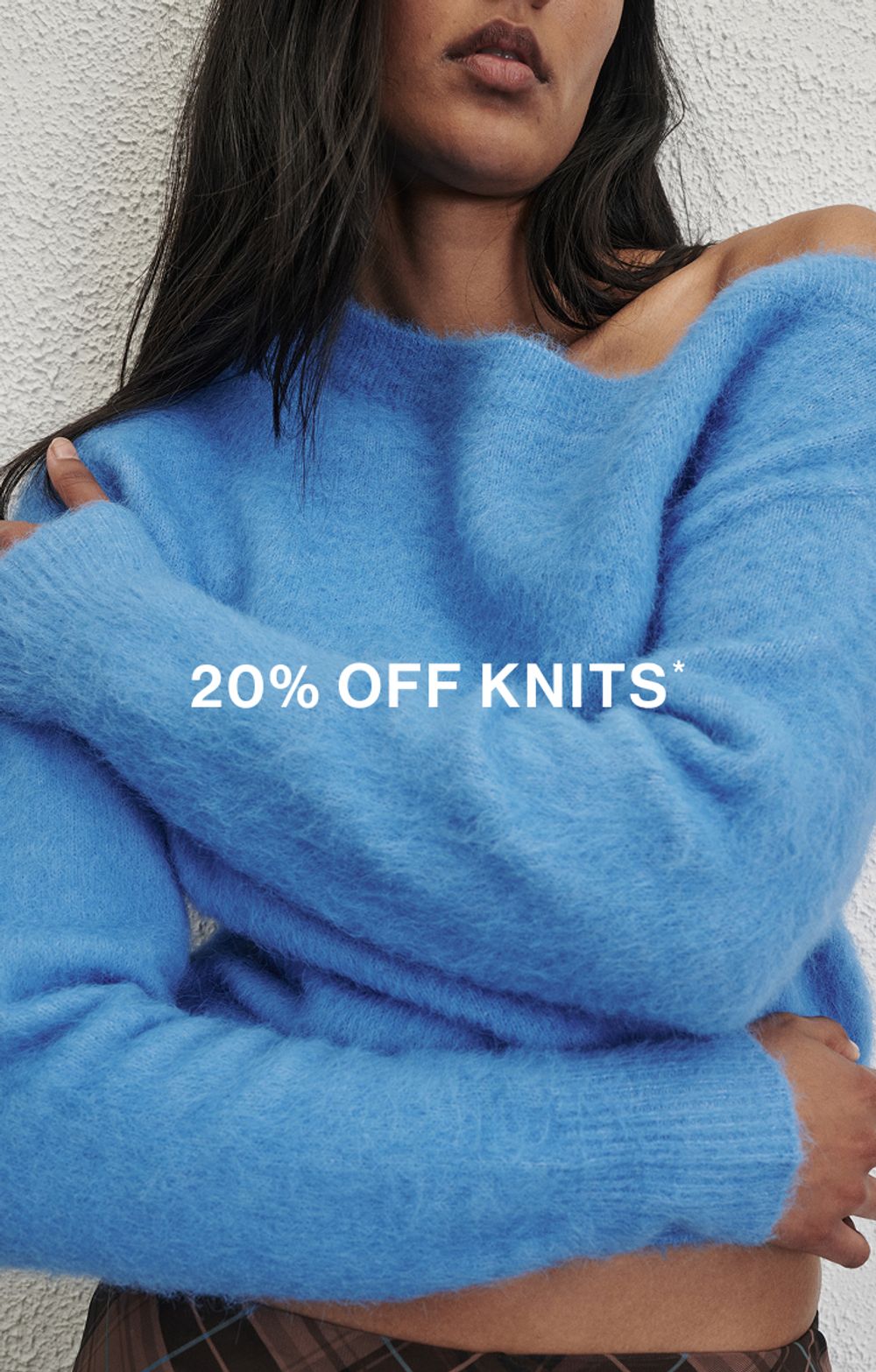 Woman in a blue knit in front of a white wall with text that reads "20% off all Knits"