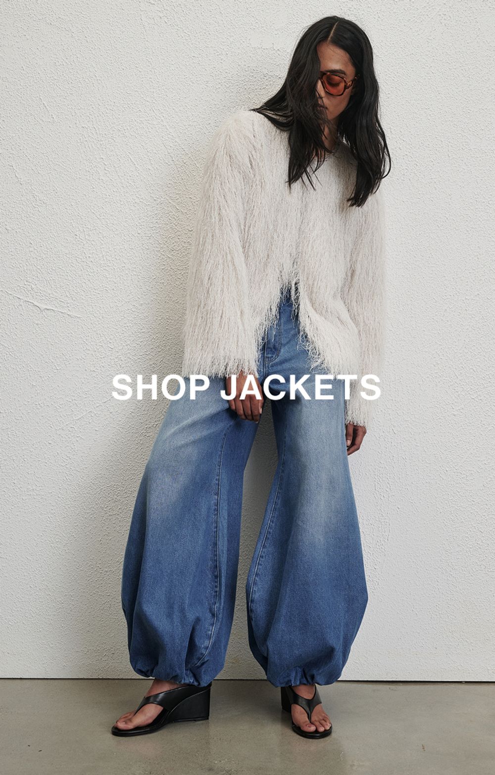 Woman posing in front of a white wall wearing a jeans and a black long sleeve top with text that states "20% off all denim"