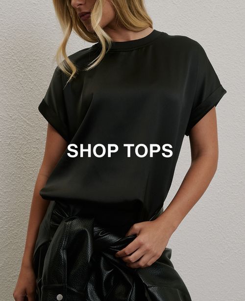 Woman posing in front of a white wall wearing a jeans and a black long sleeve top with text that states "20% off all denim"