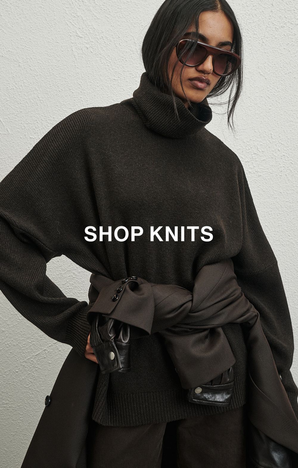 Woman in a blue knit in front of a white wall with text that reads "20% off all Knits"