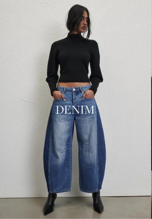 Woman posing in front of a white wall wearing a jeans and a black long sleeve top with text that states "denim"