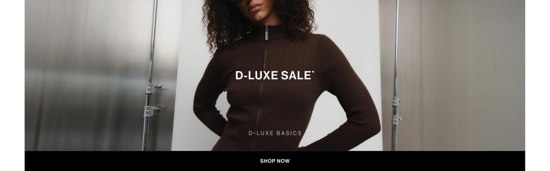 Model in a brown zip up jacket standing in front of a white wall with text overlay which states "FURTHER 30% OFF DLUXE BASICS"