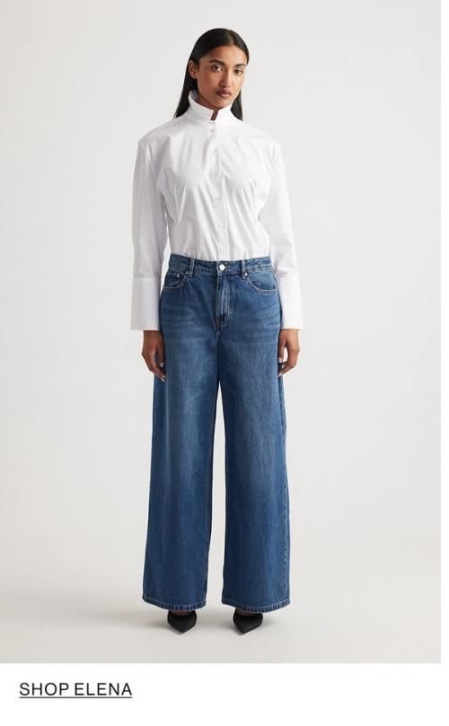 Woman standing in front of a white wall wearing a white shirt and wide jeans, with overlaid text that reads “Shop Elena.”