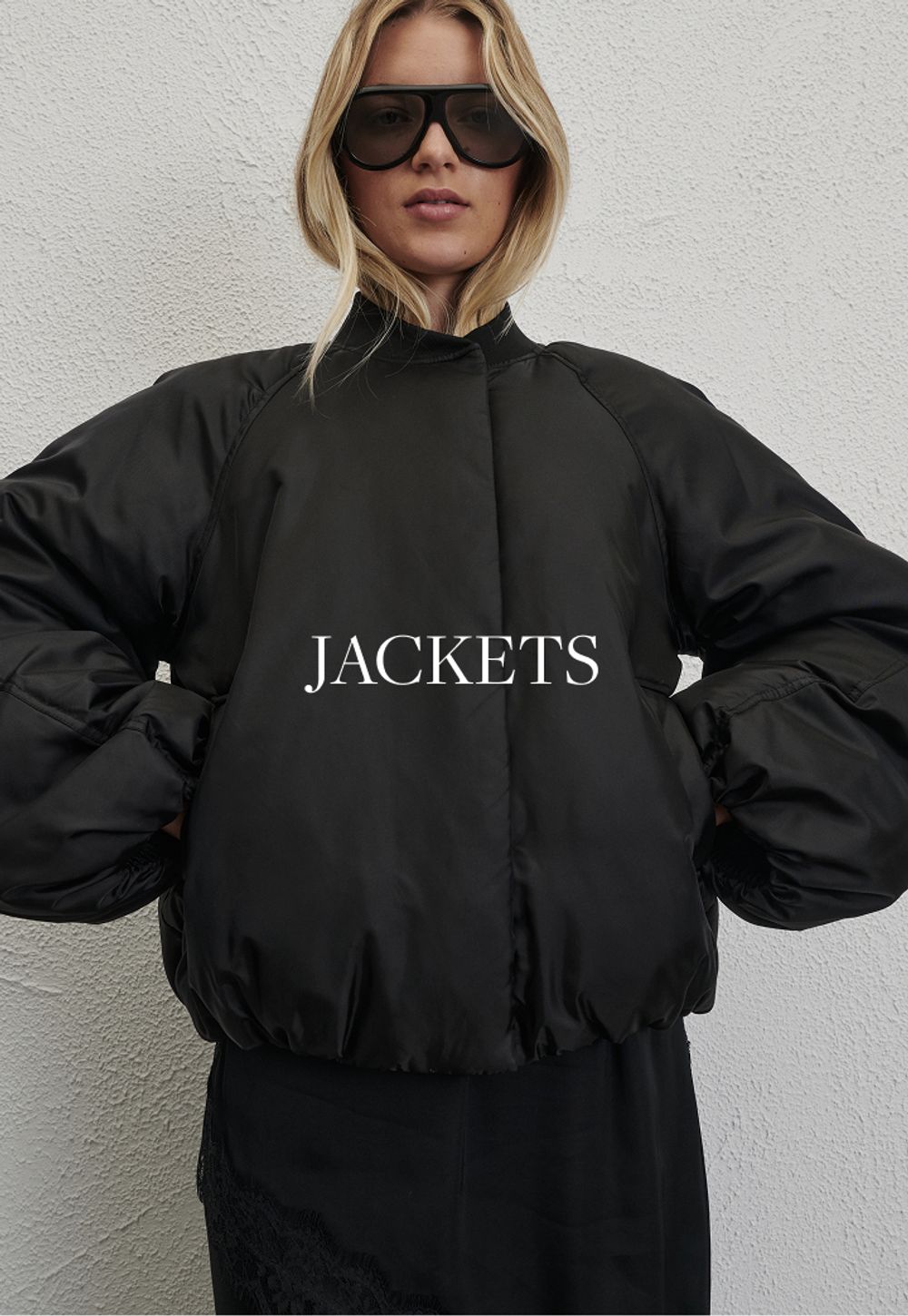 Woman sitting in front of a white wall wearing black jacket with text overlay which states "Jackets"