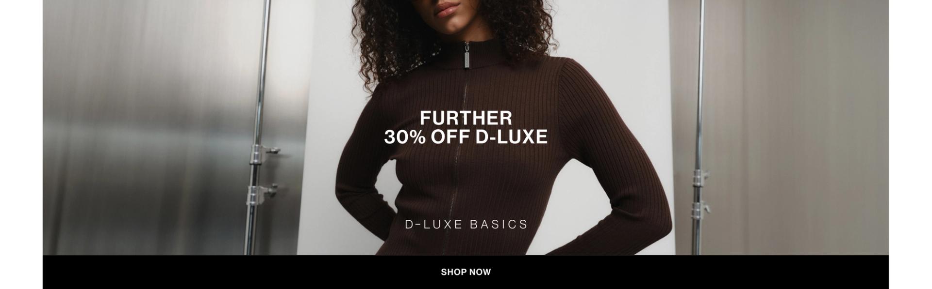 Model in a brown zip up jacket standing in front of a white wall with text overlay which states "FURTHER 30% OFF DLUXE BASICS"