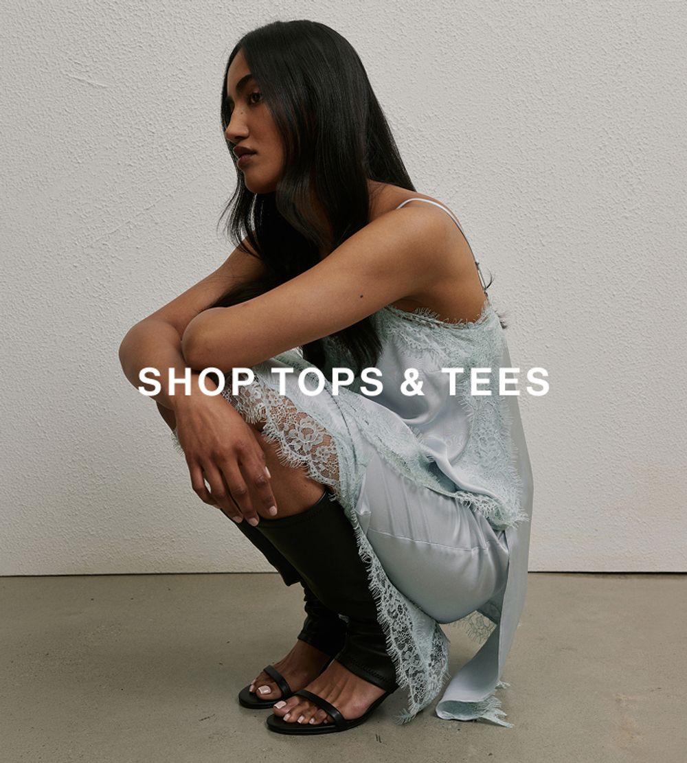 Woman posing in front of a white wall, crouching down wearing a matching blue lace set with text that reads "shop tops" 