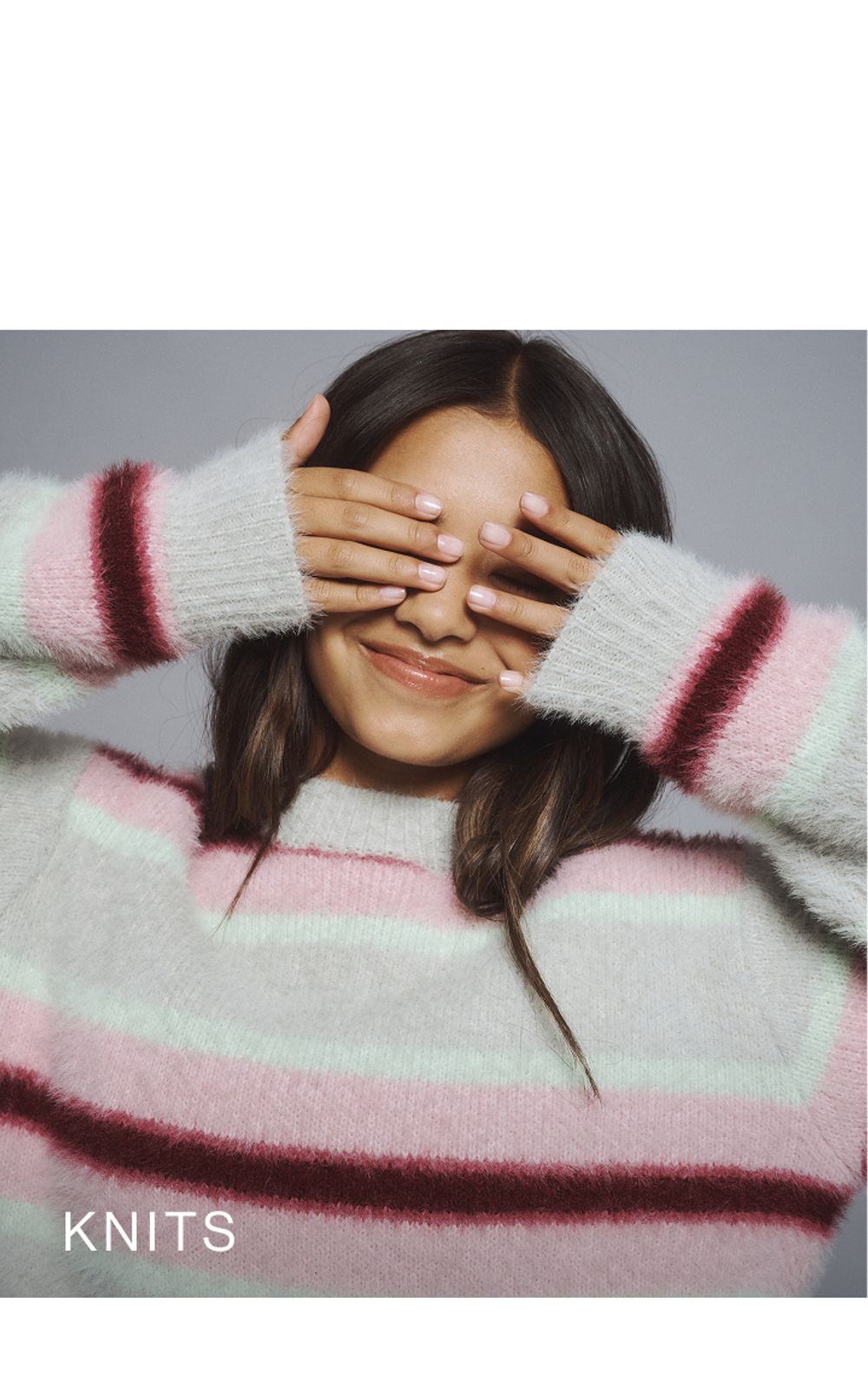 Young girl wearing a pink stripe knit cardigan. SHOP TEEN KNITWEAR.