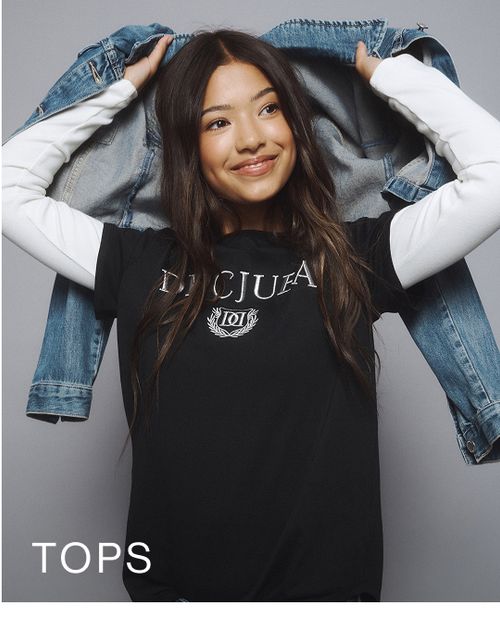 Young girl wearing a black Decjuba tee layered over a white long sleeve top. SHOP TEEN TOPS.