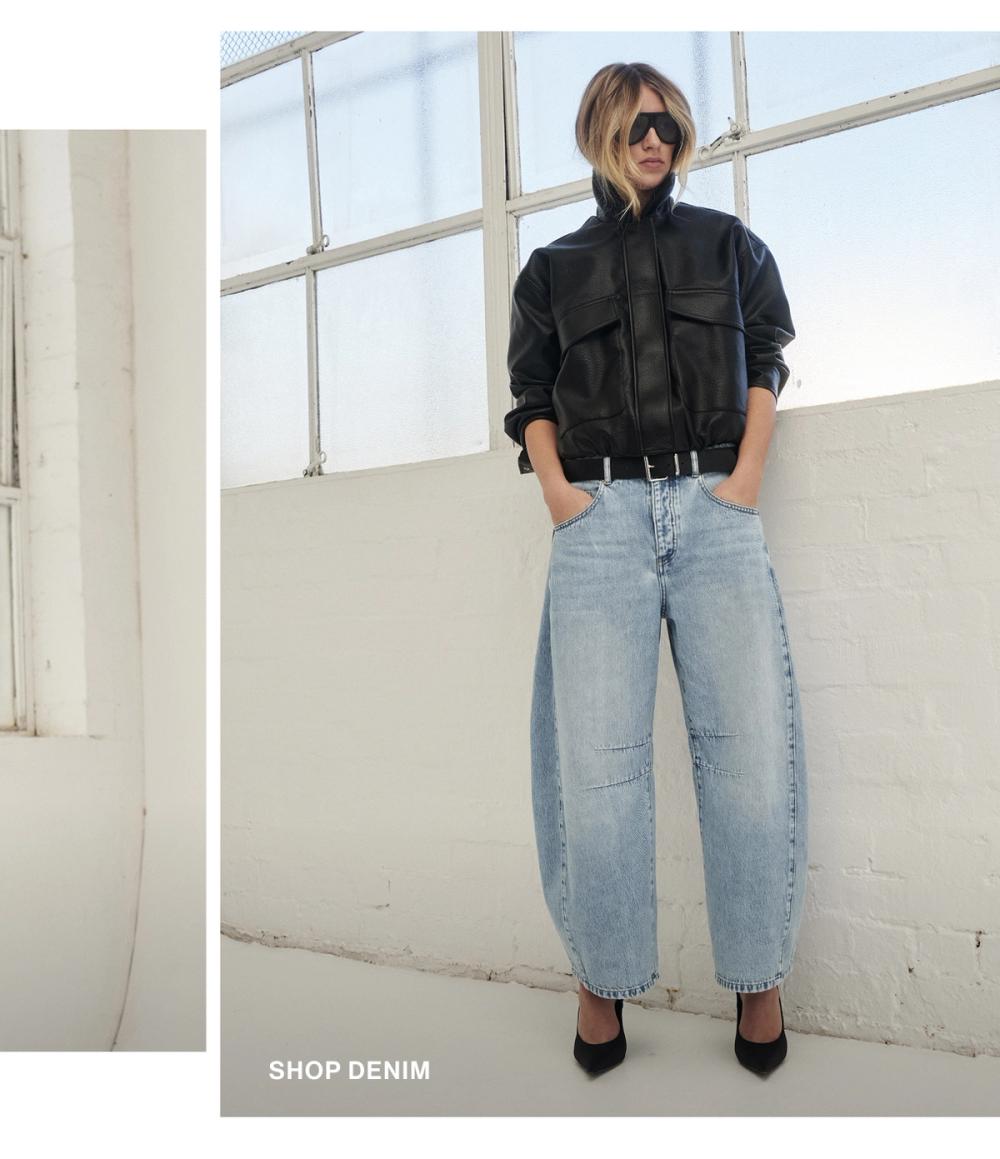 Model posing in a pair of light blue barrel denim jeans with a black jacket. SHOP DENIM