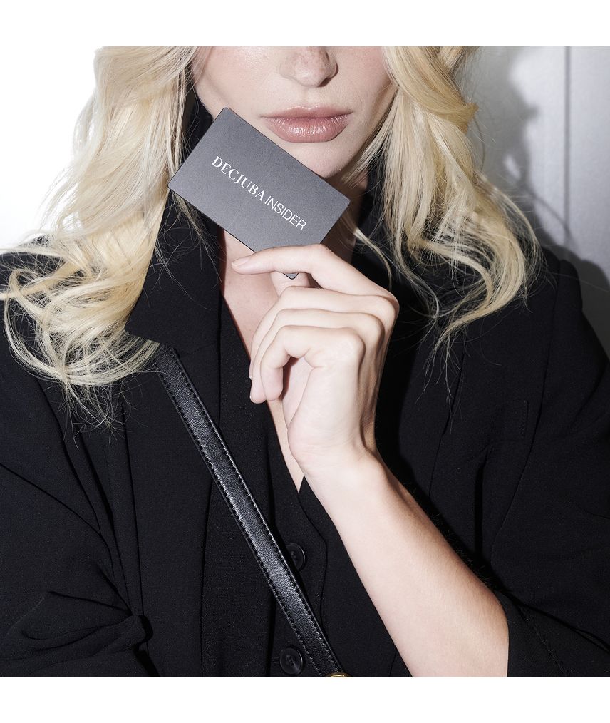 A woman with wavy blonde hair holds a dark "DECJUBA INSIDER" loyalty card, wearing a black outfit.