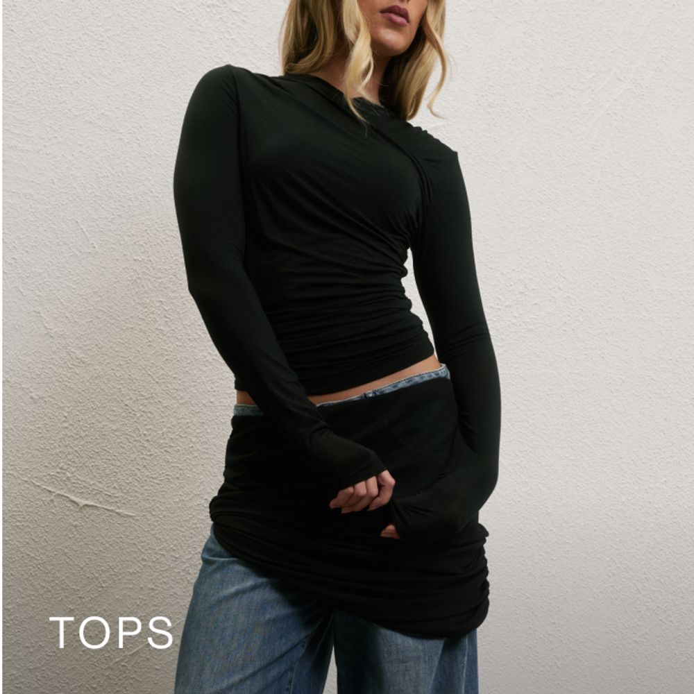 Model wearing a black long sleeve top. SHOP TOPS.