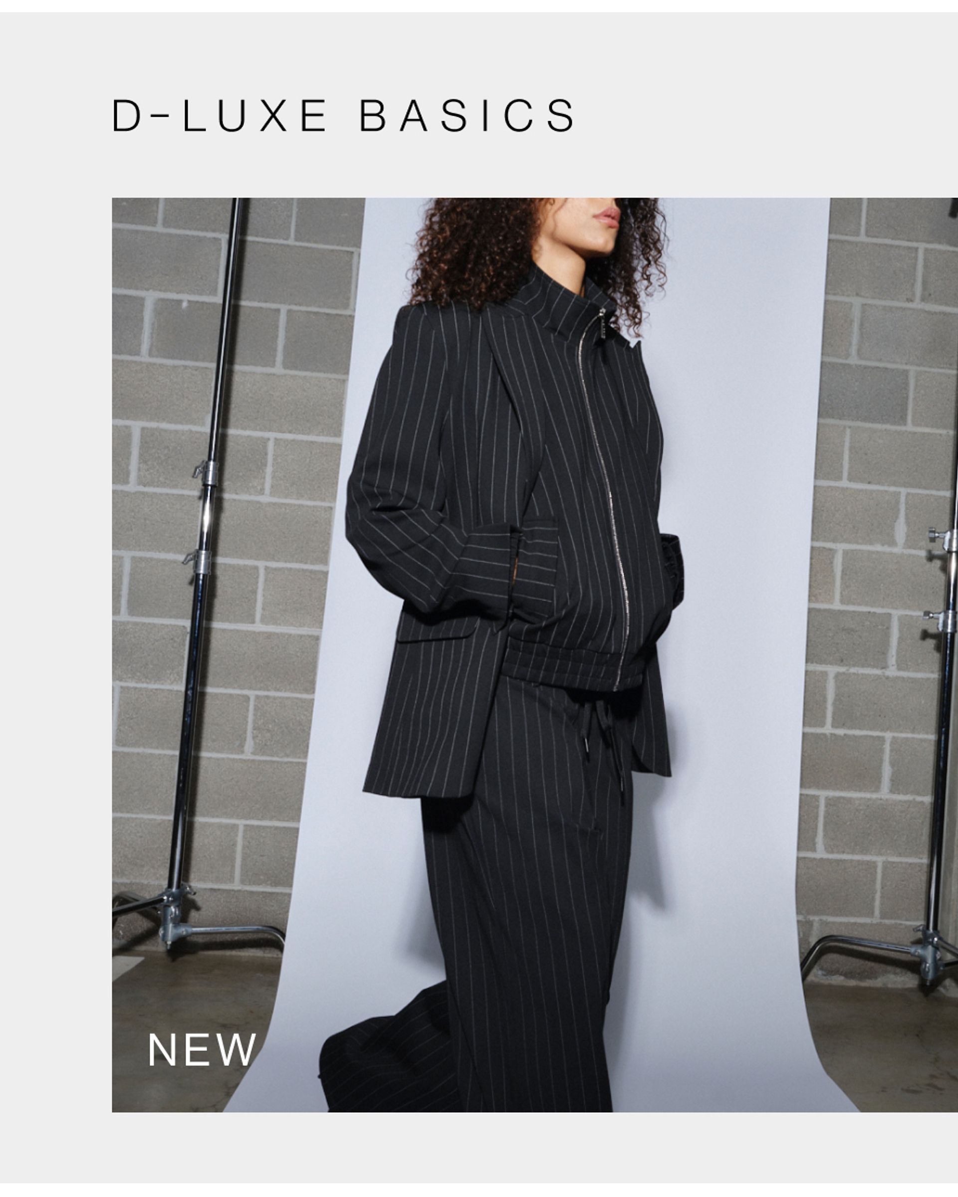 Model wearing black pinstripe suit in a studio. SHOP NEW D-LUXE.