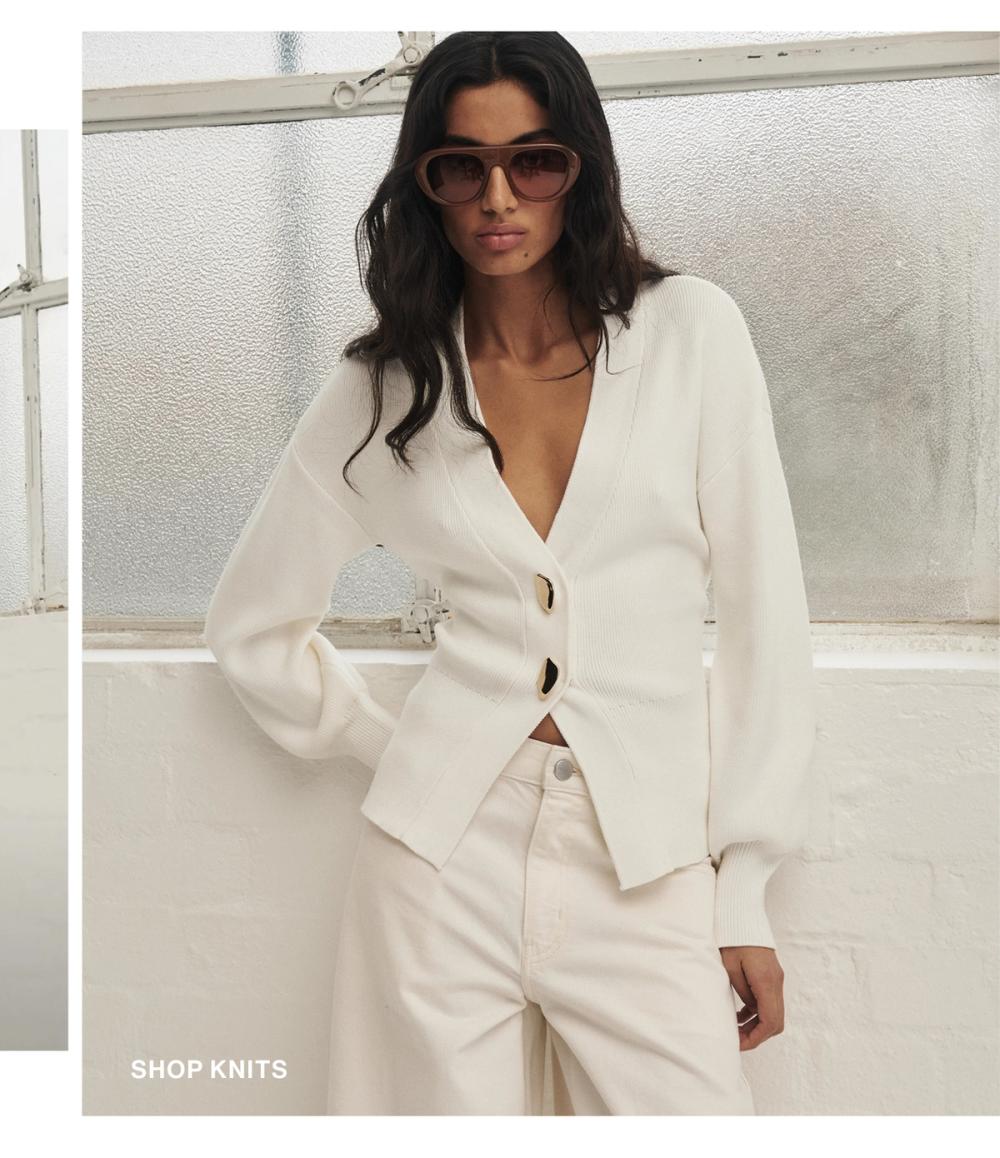Model posing on a white knit cardigan. SHOP KNITS.