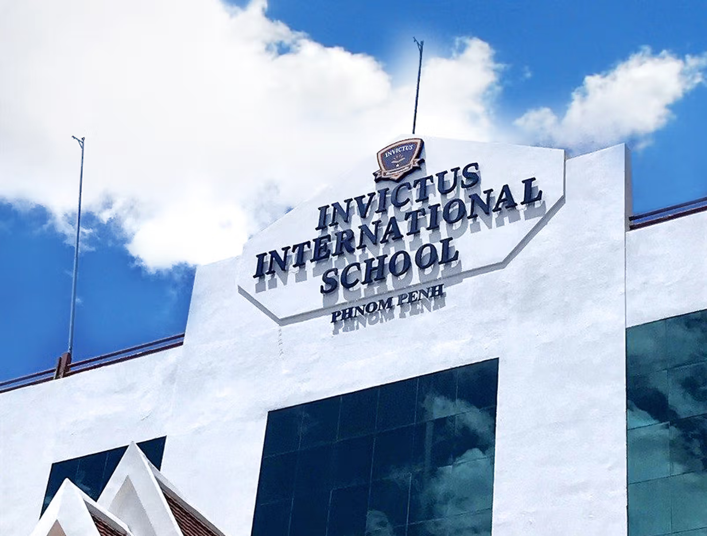 Front facade of Invictus International School’s Phnom Penh Campus in Cambodia, featuring a striking white building with angular architectural elements, large tinted windows, and bold school signage against a bright blue sky.