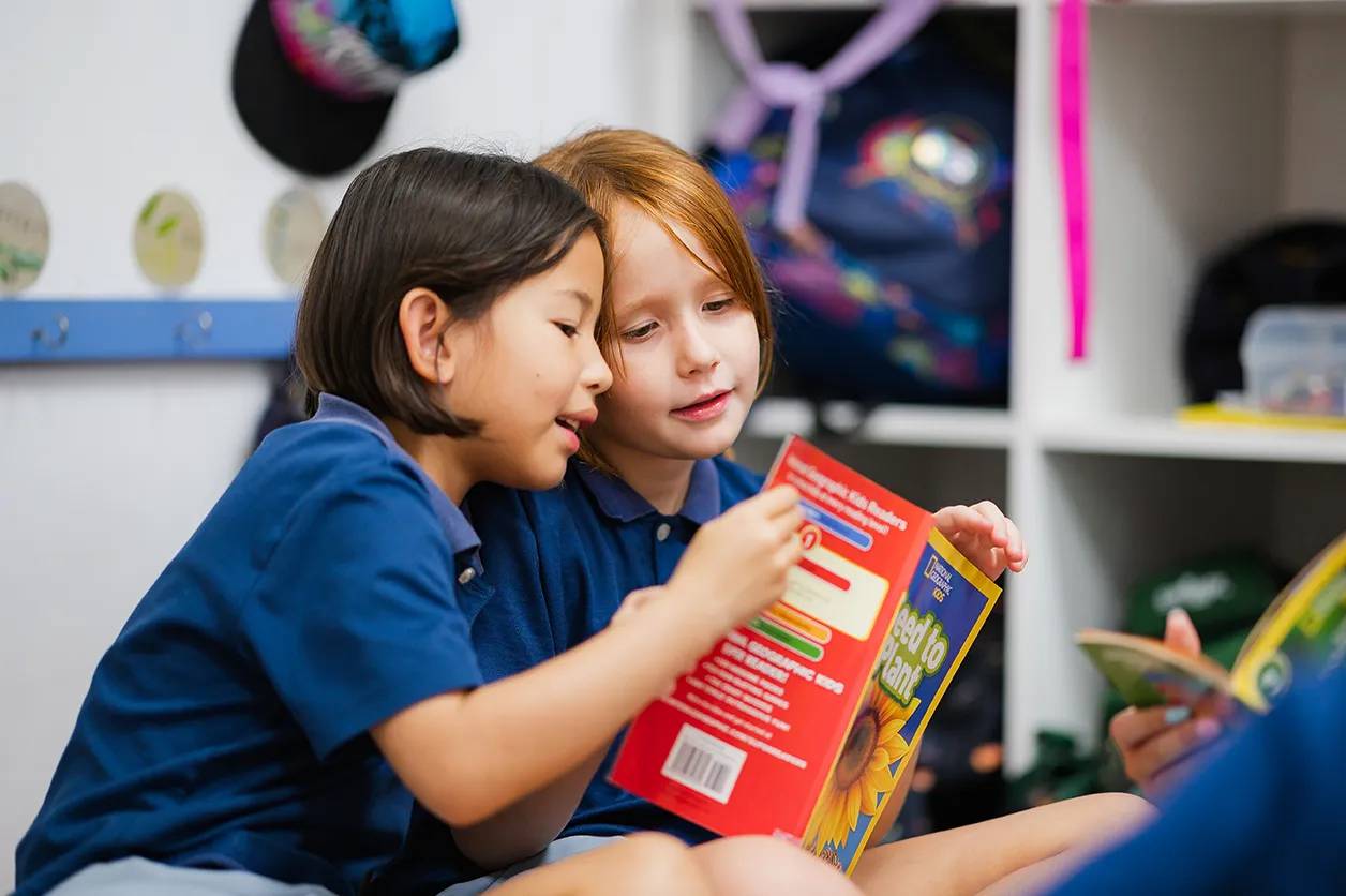 Two primary school students wearing Invictus uniform reading a book together in a modern library