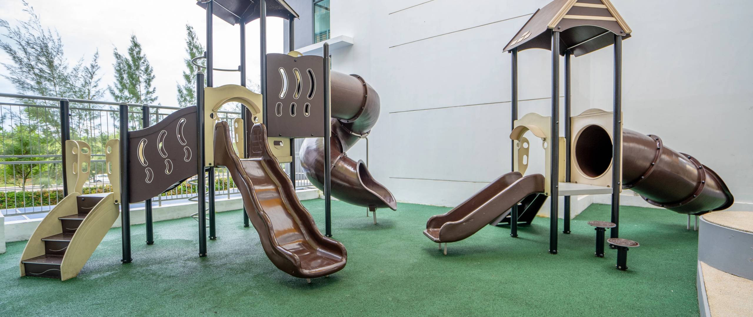 Shaded playground with slides, climbing frames, and safety flooring.